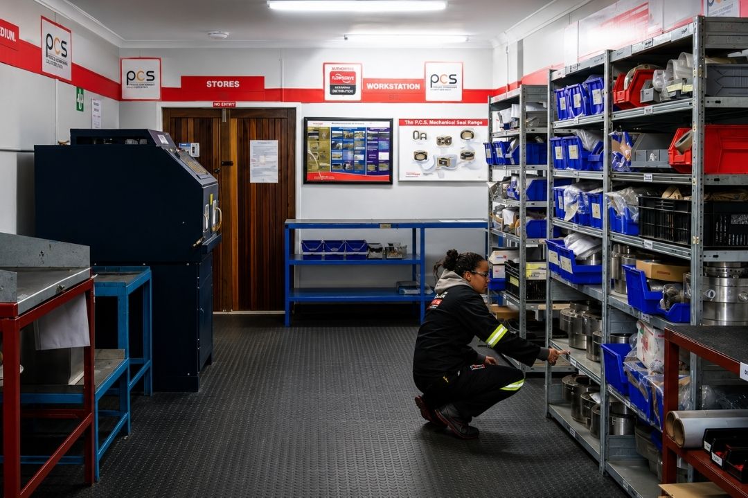Organised PCS workshop stores and inspection area with shelving, industrial components and a technician selecting parts for maintenance and repair work.